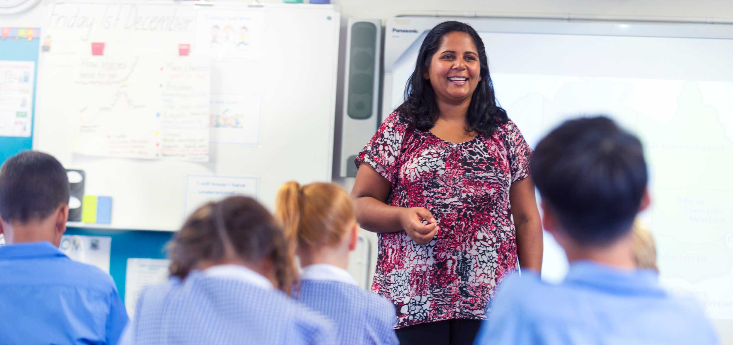 A teacher stands at the front of the classroom, talking to her students.