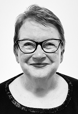 A black and white portrait of Dr Anne Kennedy. She wears a black top and glasses and is smiling with her eyes. 
