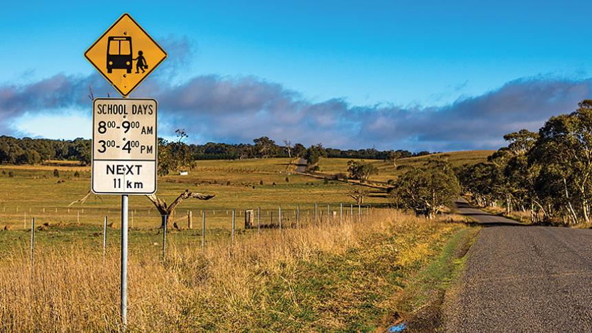 A photograph of an Australian country road and landscape, with a road sign indicating school bus times. 