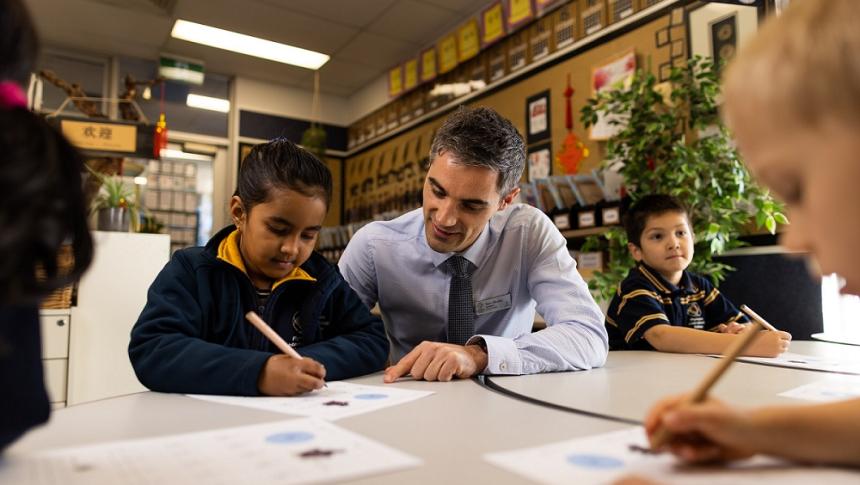 A young girl and a male teacher sitting at a desk and looking over and discussing her work. 