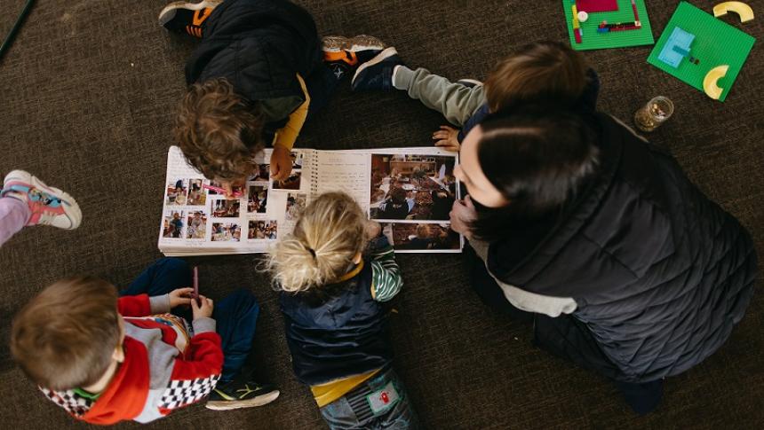 A view from above of children in a early learning setting on the floor looking at a handwritten book with images. 