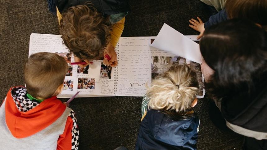 A view from above of children in a early learning setting on the floor looking at a handwritten book with images. 