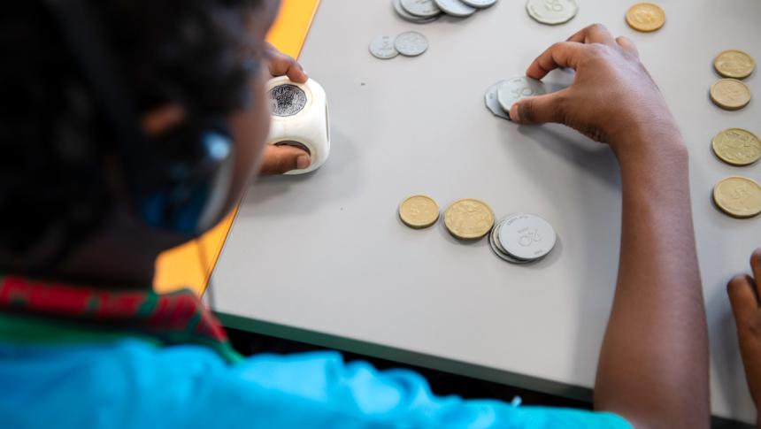 A photograph from behind of a young boy counting plastic coins. 