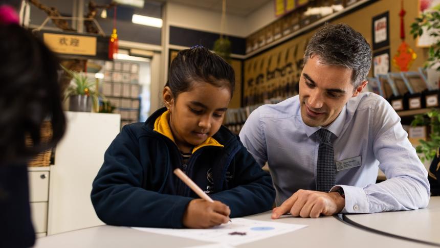A teacher and primary school student sitting at a table looking at the student's work. 