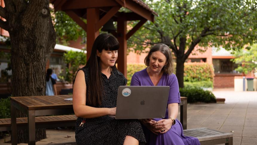 two adults on a bench looking at a laptop