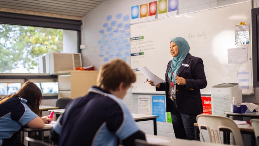 A teacher stands at the front of a class, talking. 