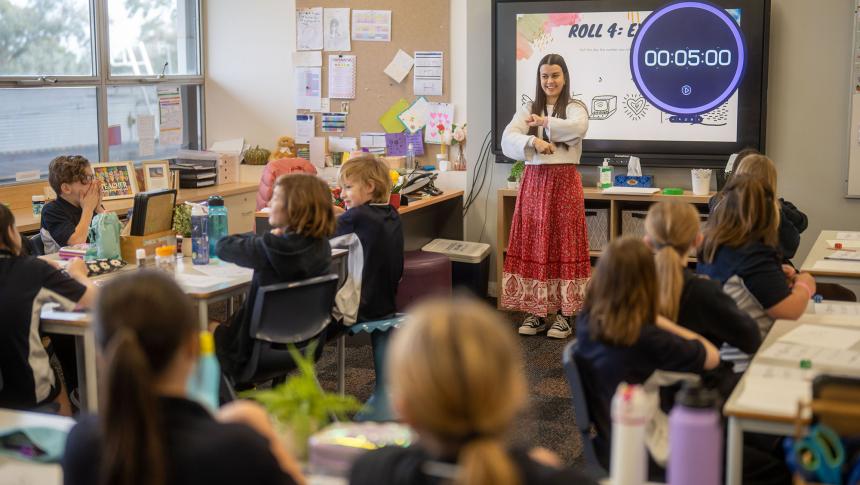 A primary teacher uses non-verbal communication with her class who are seated at their desks