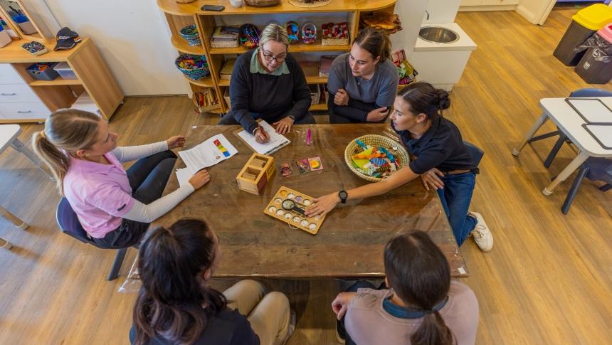 A group of early childhood and education teachers sit around a table discussing learning resources