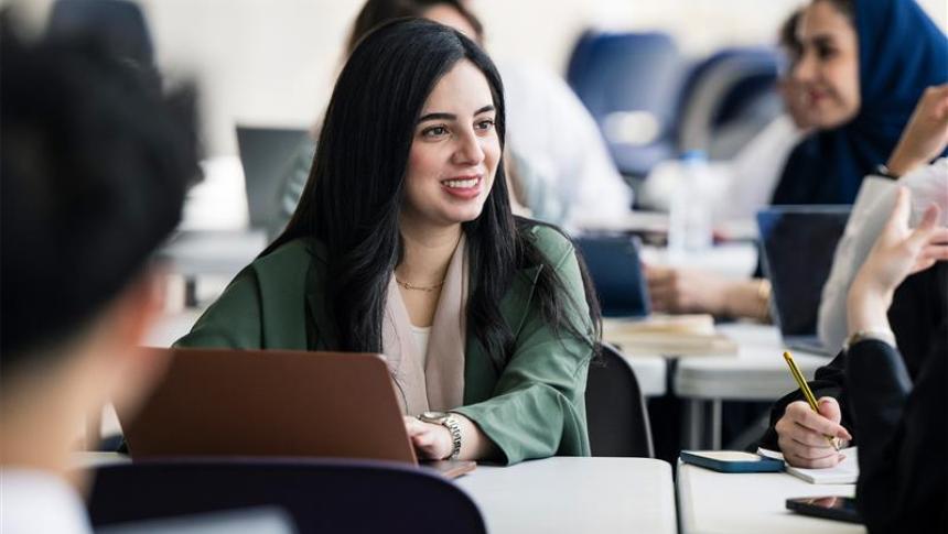 A group of teachers sit around a desk having a discussion, they have laptops and notepads next to them