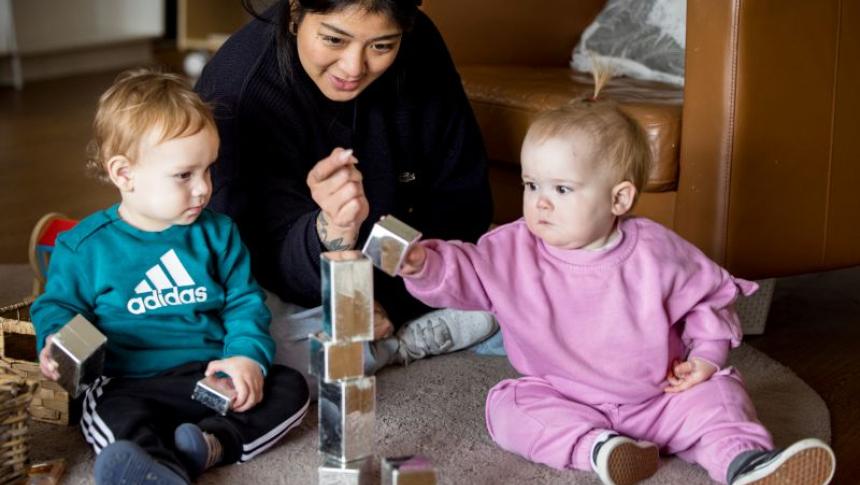 An early childhood educator sits on a mat with two young children stacking blocks to make a tower