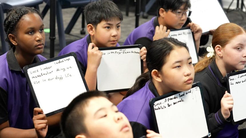 Primary school students sitting on the floor of a classroom, holding whiteboards