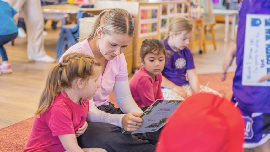 An early childhood educator sits on the floor in her classroom helping a child with reading