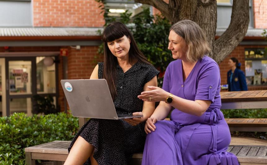 Two educators are discussing research materials on a laptop.