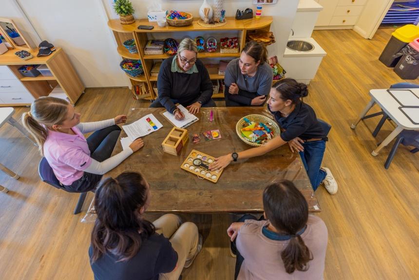 A group of early childhood and education teachers sit around a table discussing learning resources