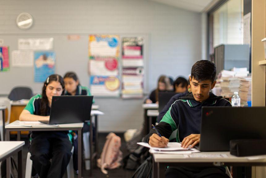 Secondary school students sit at their desks working on their laptops during a lesson