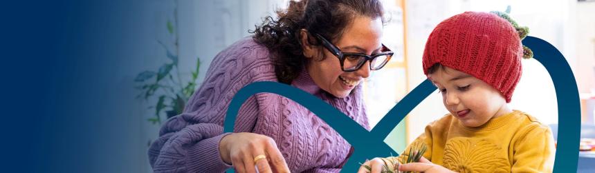 An early childhood educator with a young child in a classroom, examining a plant