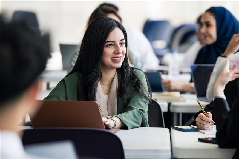 A group of teachers sit around a desk having a discussion, they have laptops and notepads next to them