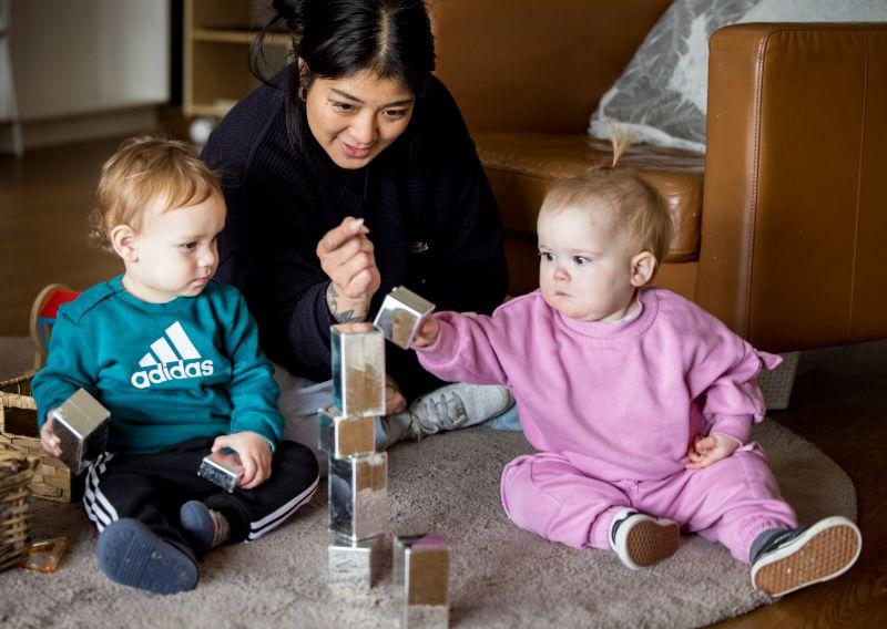 An early childhood educator sits on a mat with two young children stacking blocks to make a tower