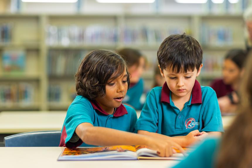 Two primary school boys sit at a desk looking through a book together