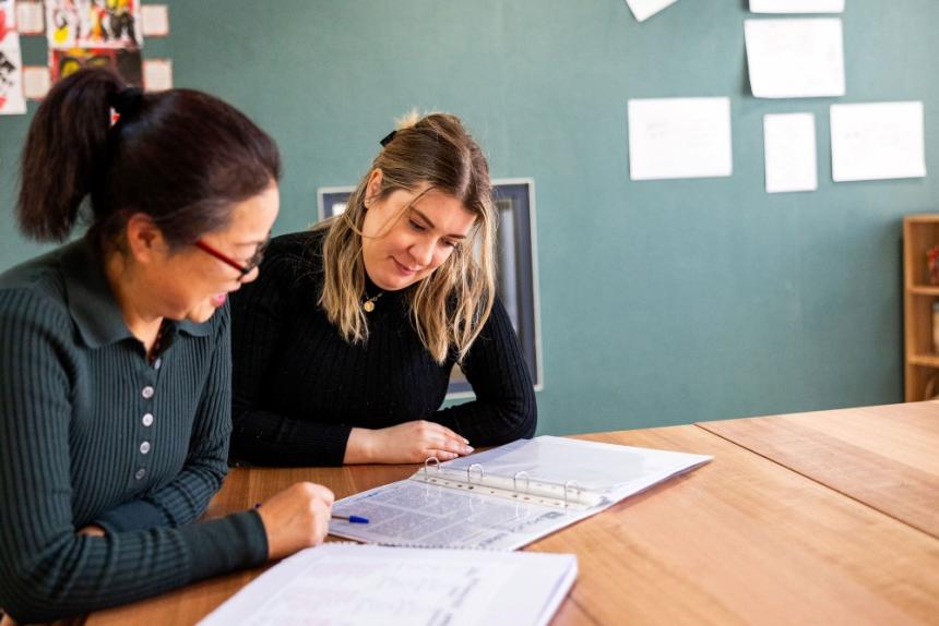Two early childhood educators sit at a table discussing a document
