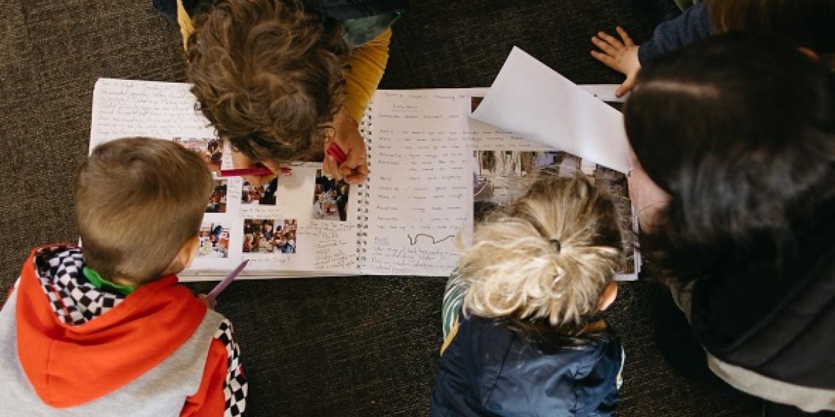 A view from above of children in a early learning setting on the floor looking at a handwritten book with images. 