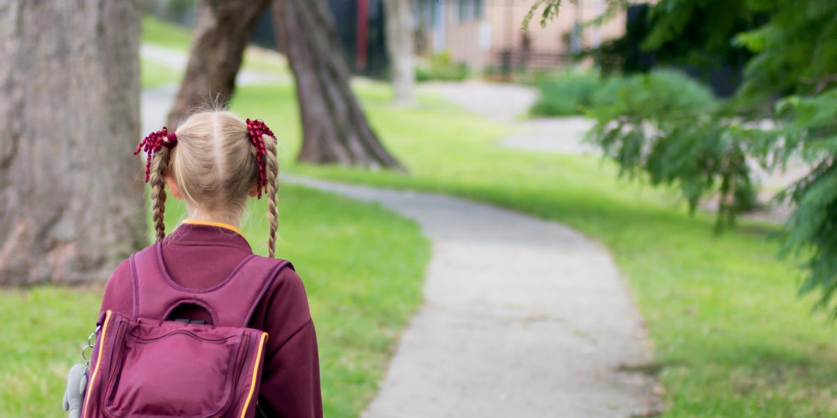 Girl in pigtails and school uniform with backpack walking home from school